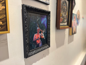 Art gallery wall with framed artworks, including a prominent painting of a figure with antlers.