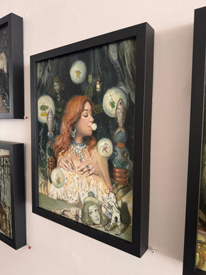 Framed artwork of a woman with red hair and decorative elements on a wall.