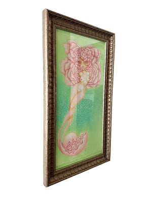 Framed artwork of a mermaid with a large pink flower on a green background, hanging on a wall.