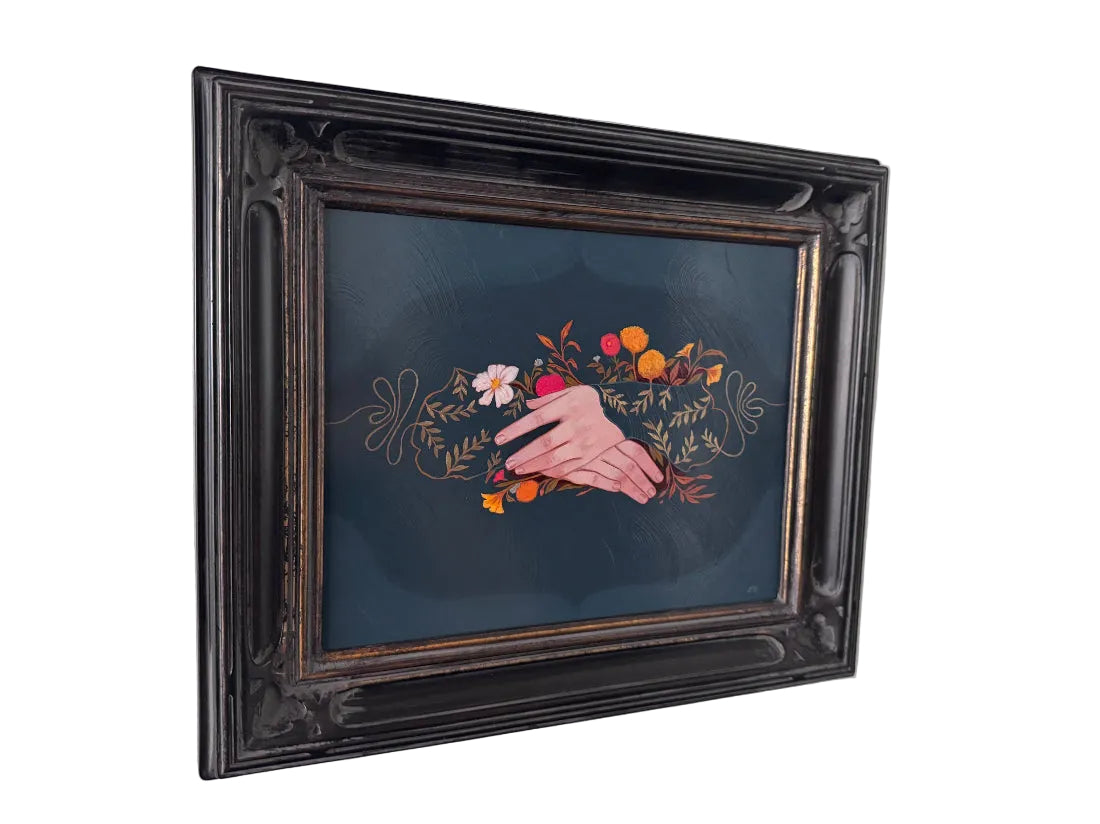 A framed painting featuring a hand painted with a floral ring, set within an ornate dark brown wooden frame and hung on a white wall.