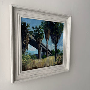 Framed painting of palm trees on a gray wall