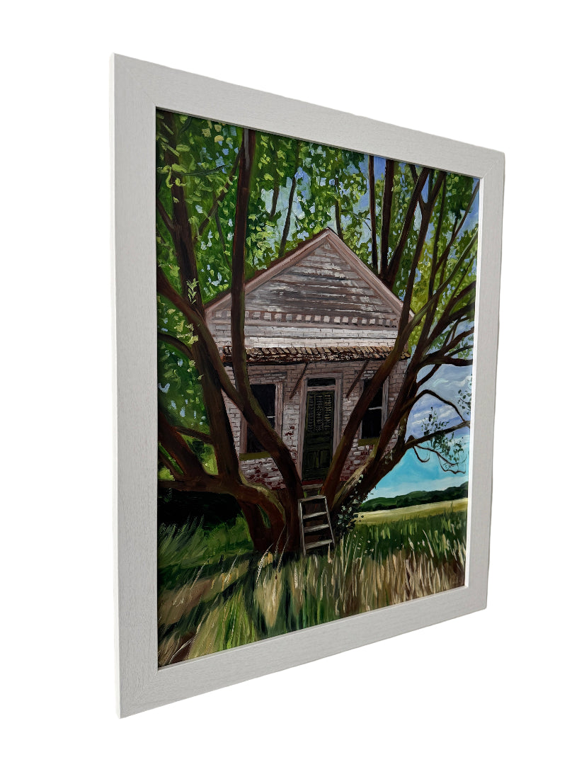 Framed artwork of a house partially obscured by trees on a white wall