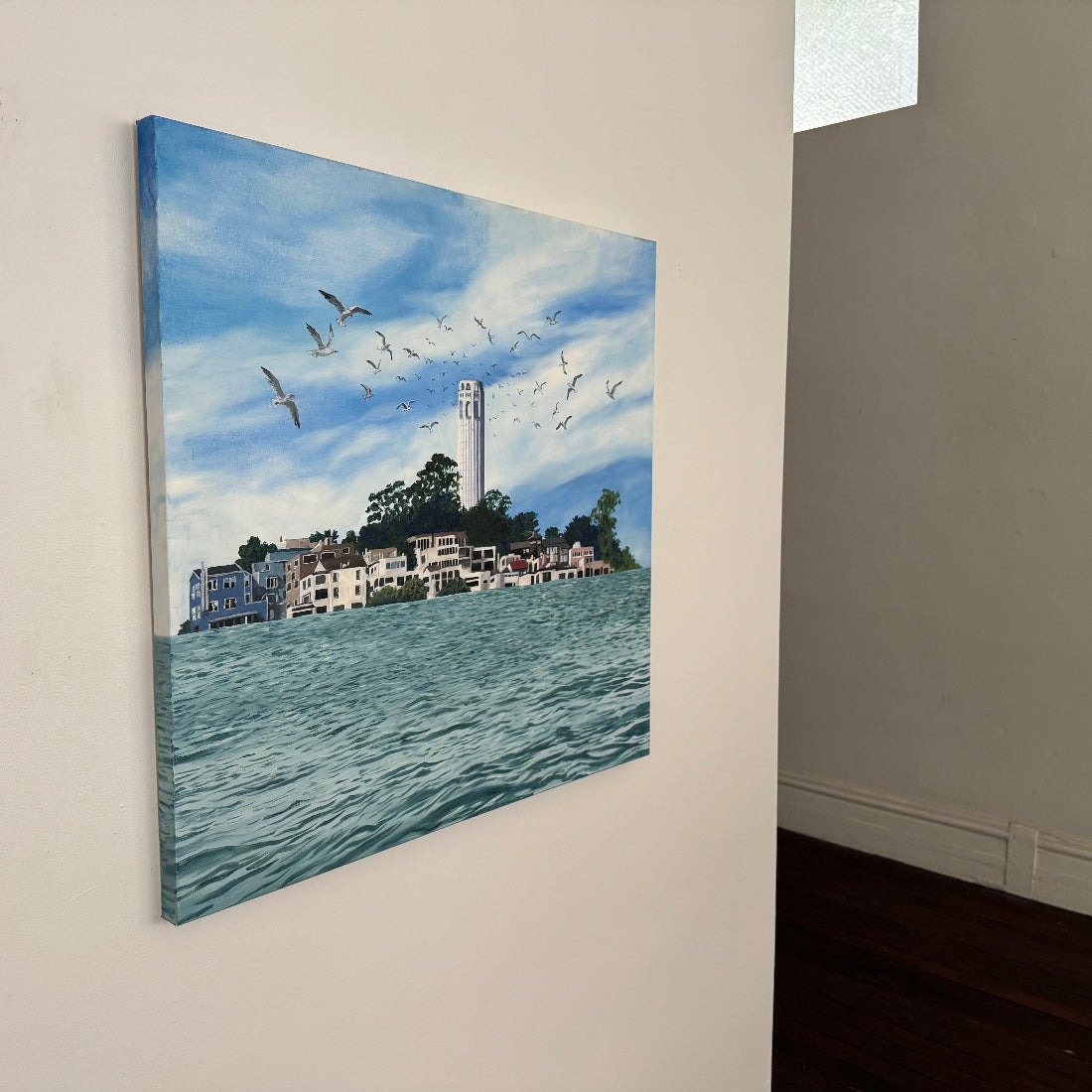 Canvas painting of a coastal scene with buildings and birds flying over water, mounted on a wall.