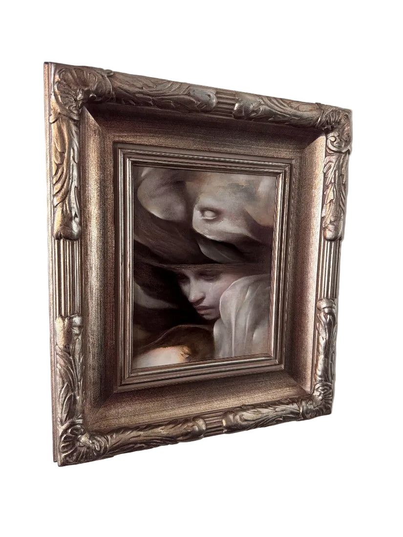 An ornate, vintage-style square picture frame with a distressed silver and gold finish, holding a classical painting of two cherub faces, shown hanging on a plain off-white wall.