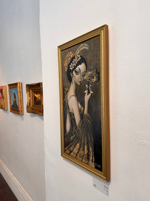 A framed vertical portrait painting hangs on a white gallery wall. The artwork depicts a woman in a dark gown holding a gold masquerade mask, with a large gold frame.
