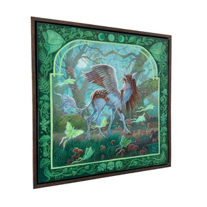 Framed artwork of a unicorn in a forest setting on a white wall.