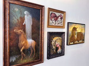 Collection of framed artworks featuring horses and other figures on a wall.