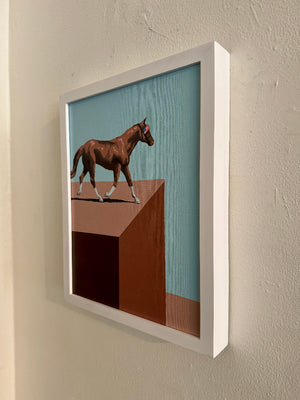 Framed artwork of a horse on a platform against a blue sky, mounted on a wall.