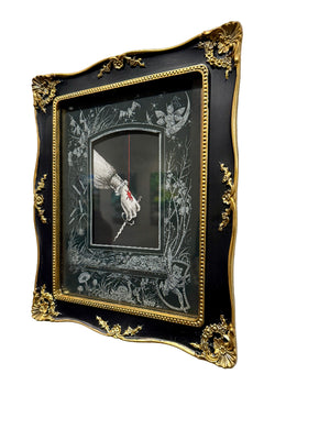 Decorative framed artwork with a gold border on a white wall.