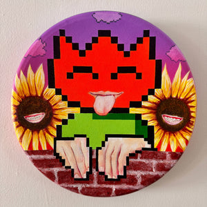 Pixelated design with a cat face, sunflowers, and a brick background on a circular object.