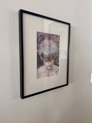 Framed artwork of a person with floral headpiece on a white wall