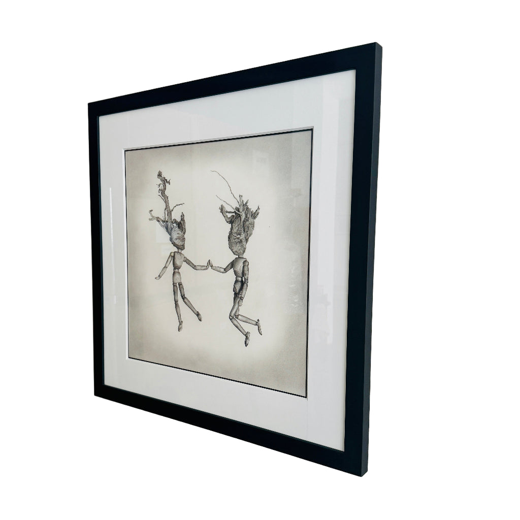 Framed artwork of two wooden figures holding hands on a white wall.
