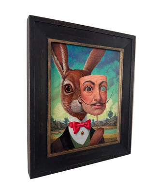 Framed artwork of a rabbit with a human face and bow tie on a white wall.