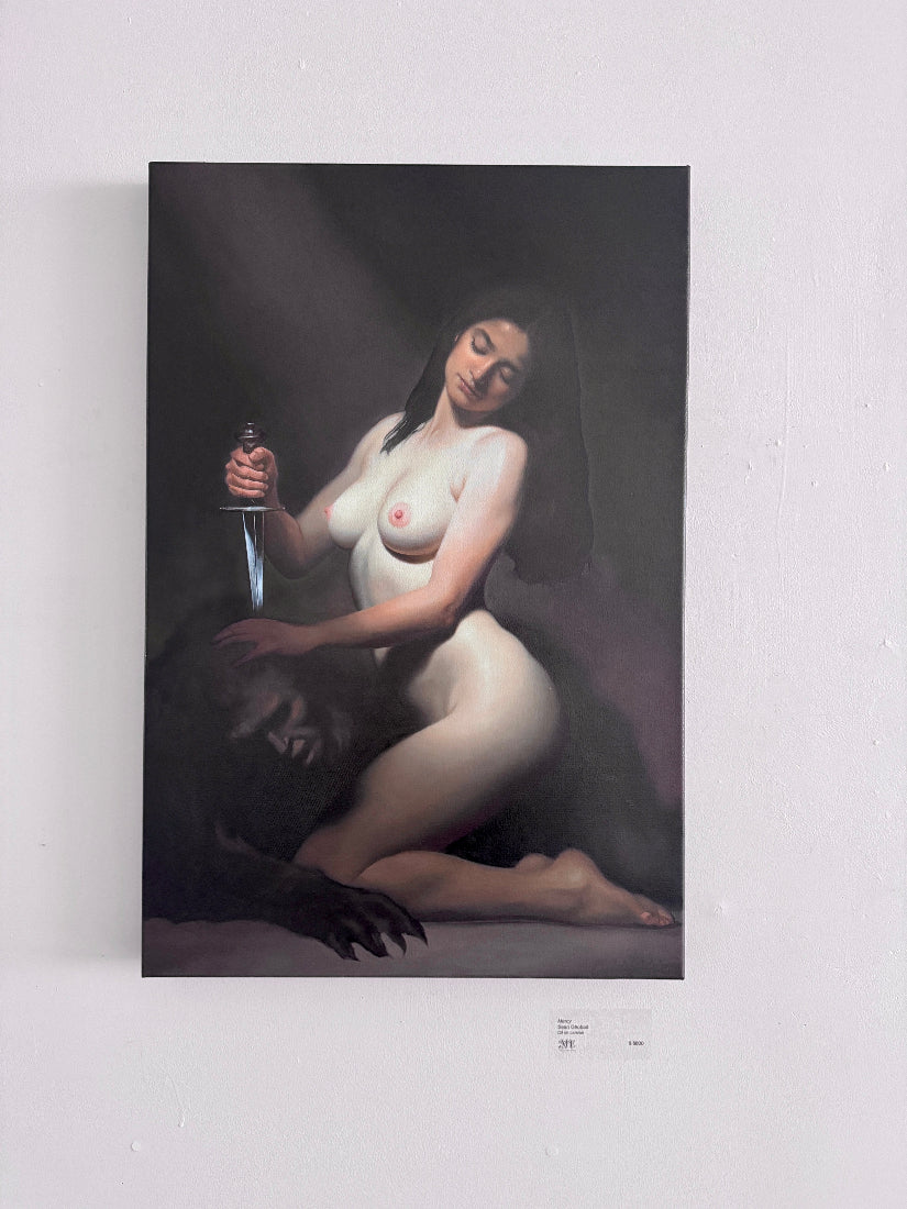 A vertical canvas art painting depicting a nude woman kneeling and holding a knife, displayed on a white wall.