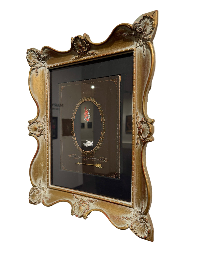 Decorative gold-framed artwork on a white wall with a small plaque below.
