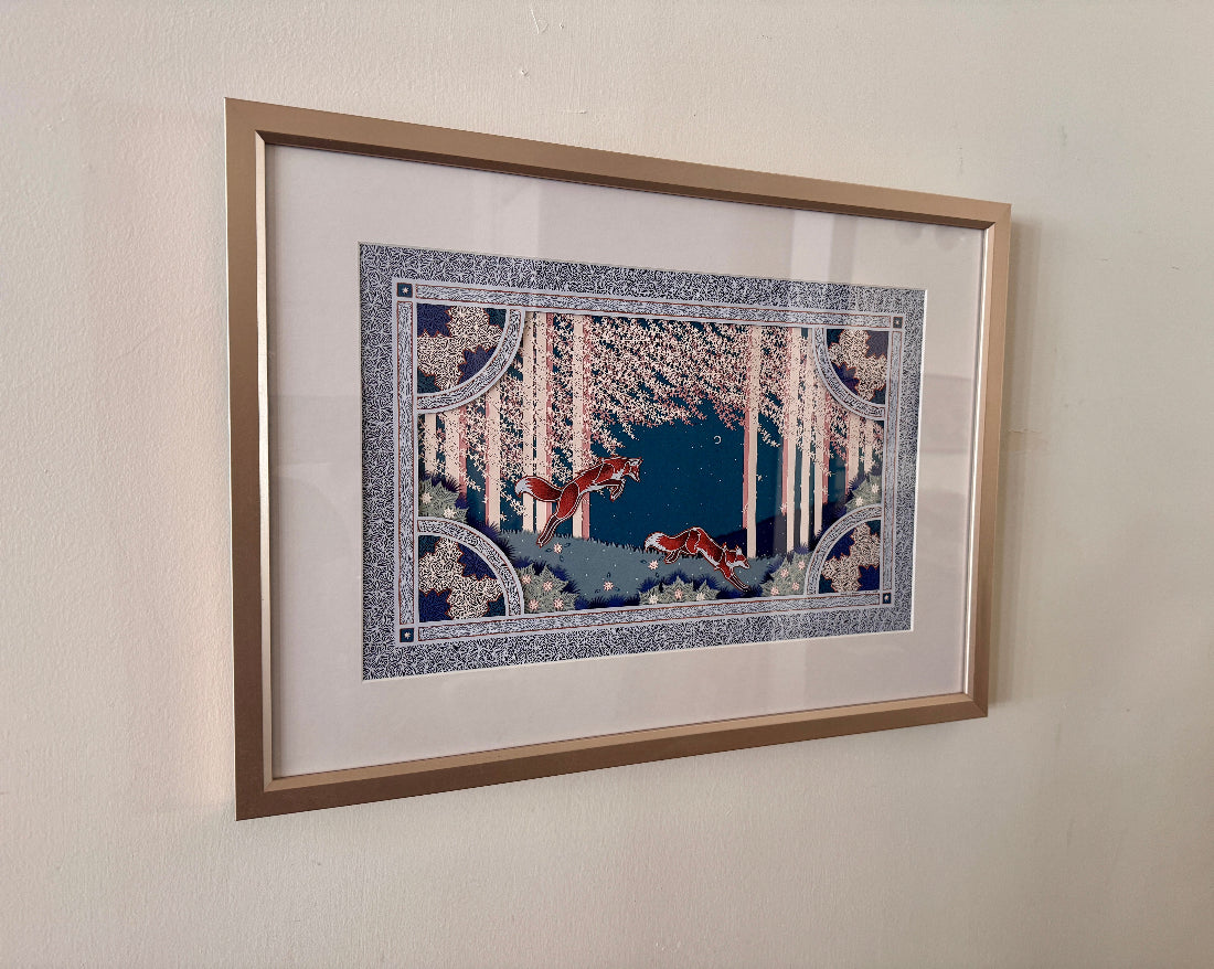 Framed artwork of two foxes in a snowy forest scene on a beige wall.