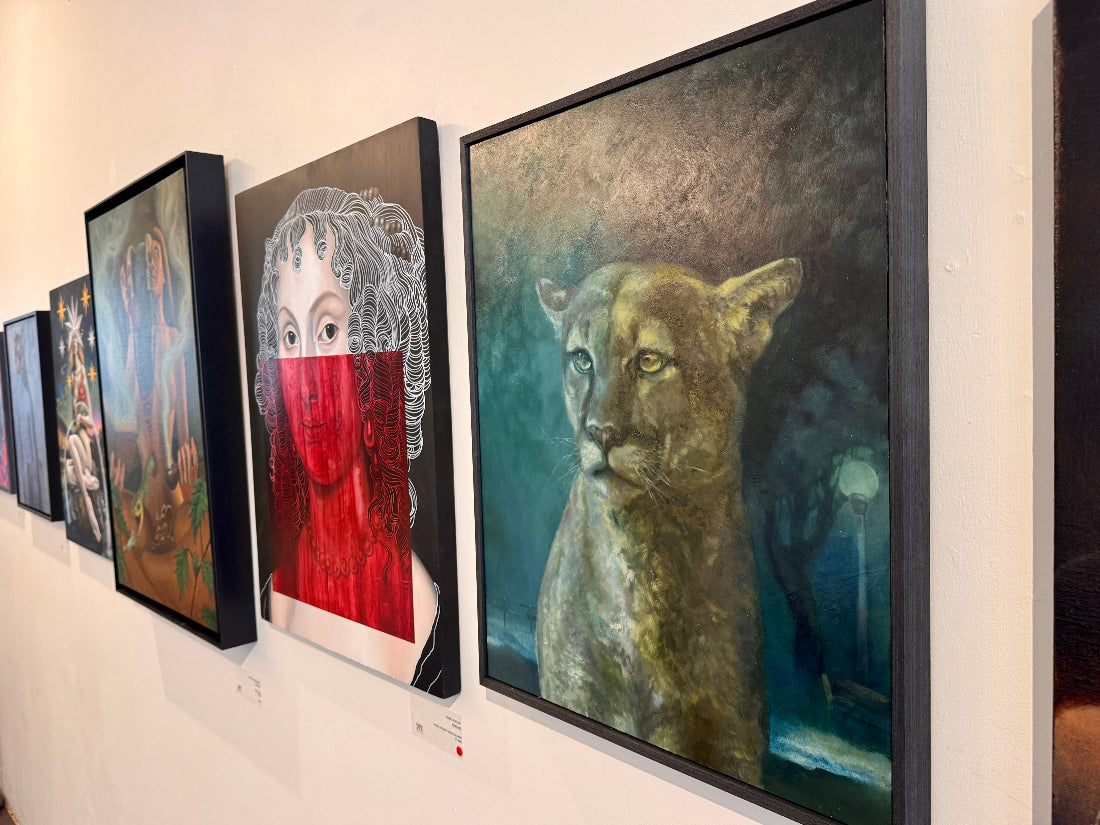 Art gallery wall with various framed artworks including a painting of a woman with red face and a panther.