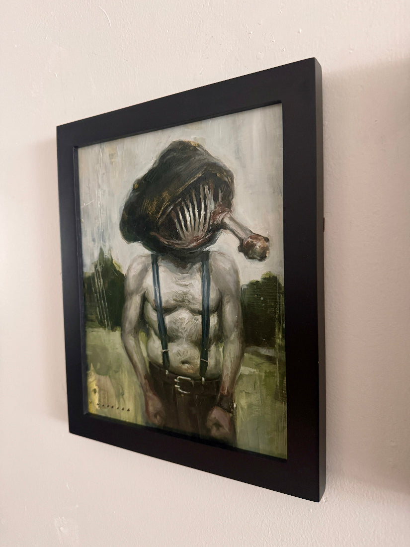 Framed artwork of a person with a creature head on a plain wall.
