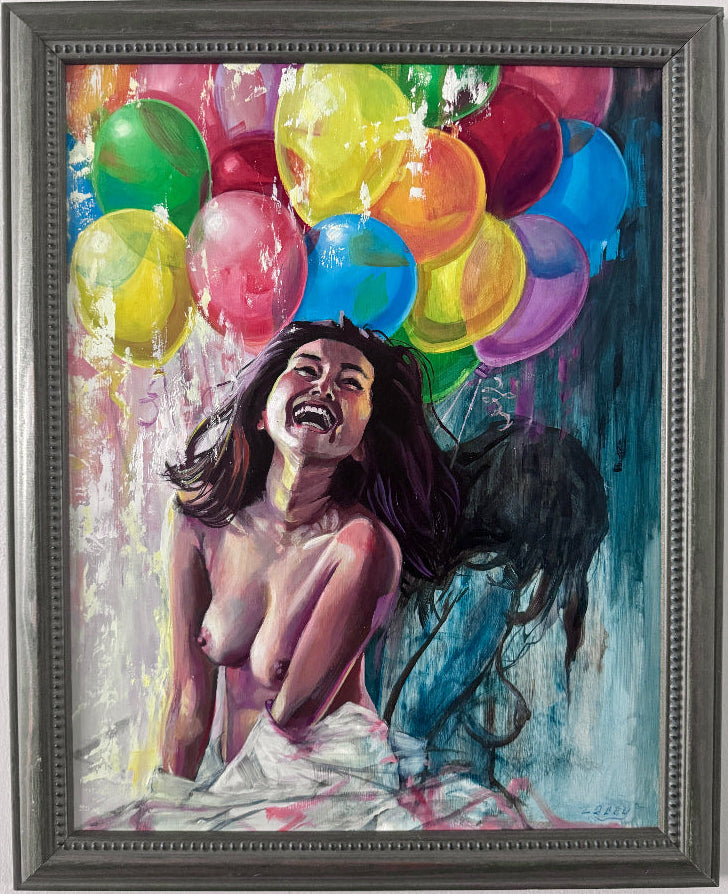 A framed painting on a white wall, depicting a laughing nude woman with dark hair surrounded by colorful balloons in yellow, green, red, blue, pink, and purple. The artwork is housed in a dark gray textured frame.