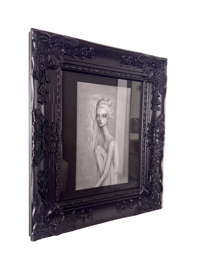 A framed black and white pencil sketch of a woman, set in an ornate black frame and mounted on a light-colored wall.