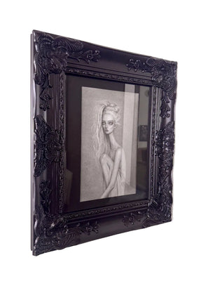 A framed black and white pencil sketch of a woman, set in an ornate black frame and mounted on a light-colored wall.