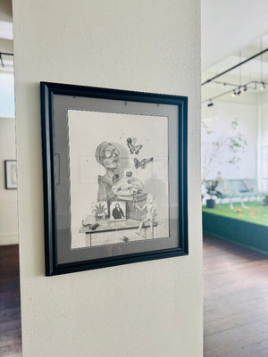 Framed black and white artwork on a wall with a view of a gallery. 