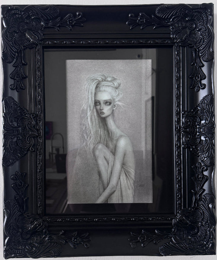 A framed black and white portrait drawing of a woman with long hair, set within an ornate black frame against a light wall.