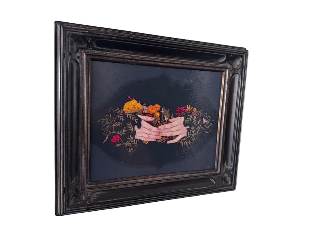 A framed painting featuring a central pink ribbon with orange and yellow flowers on a dark background, housed in an ornate black frame and mounted on a white wall.