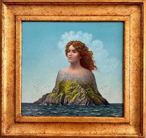 A framed surreal art print depicting a woman with red hair emerging from a rocky island into the sea under a blue sky, enclosed in a textured gold frame and mounted on a light gray wall.