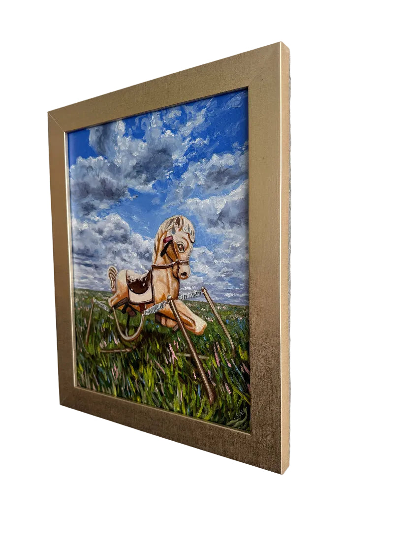 Framed artwork of a riding horse sitting in grass with a blue sky background on a white wall.