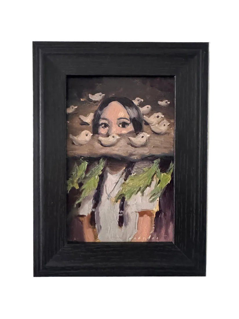 Framed painting of a stylized face with a black frame on a white brick wall.