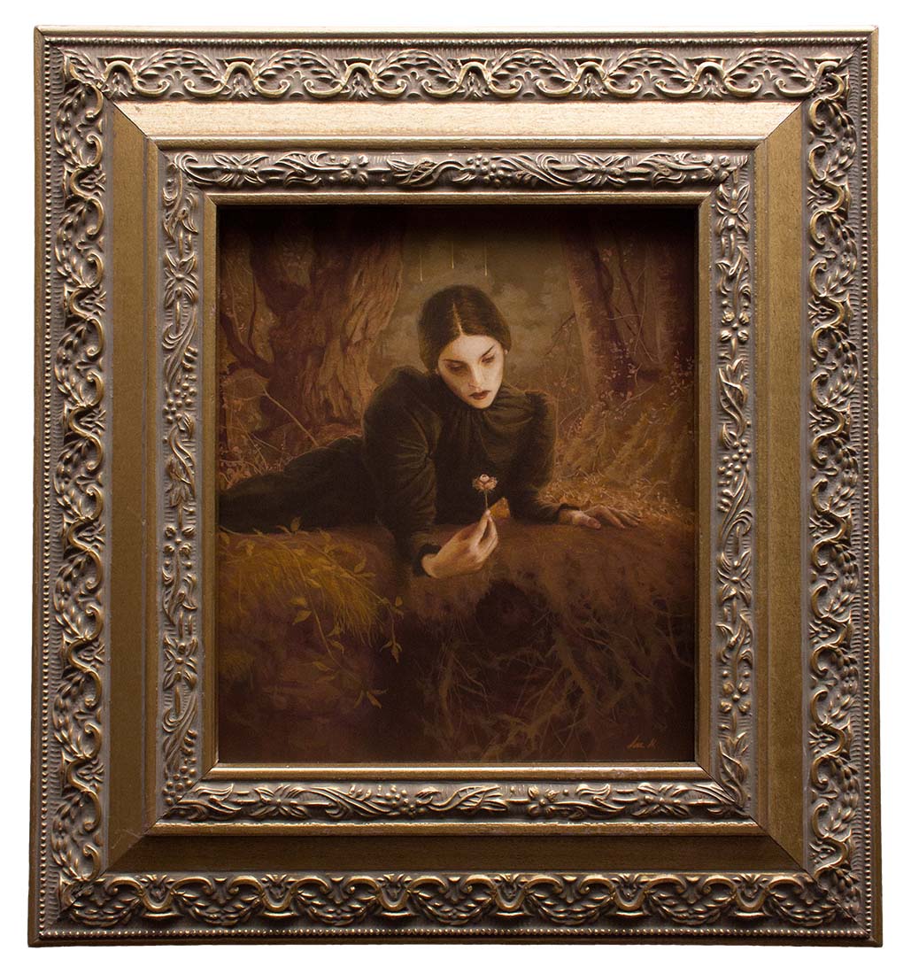 Woman in a dark coat sitting in a forest, holding a flower.