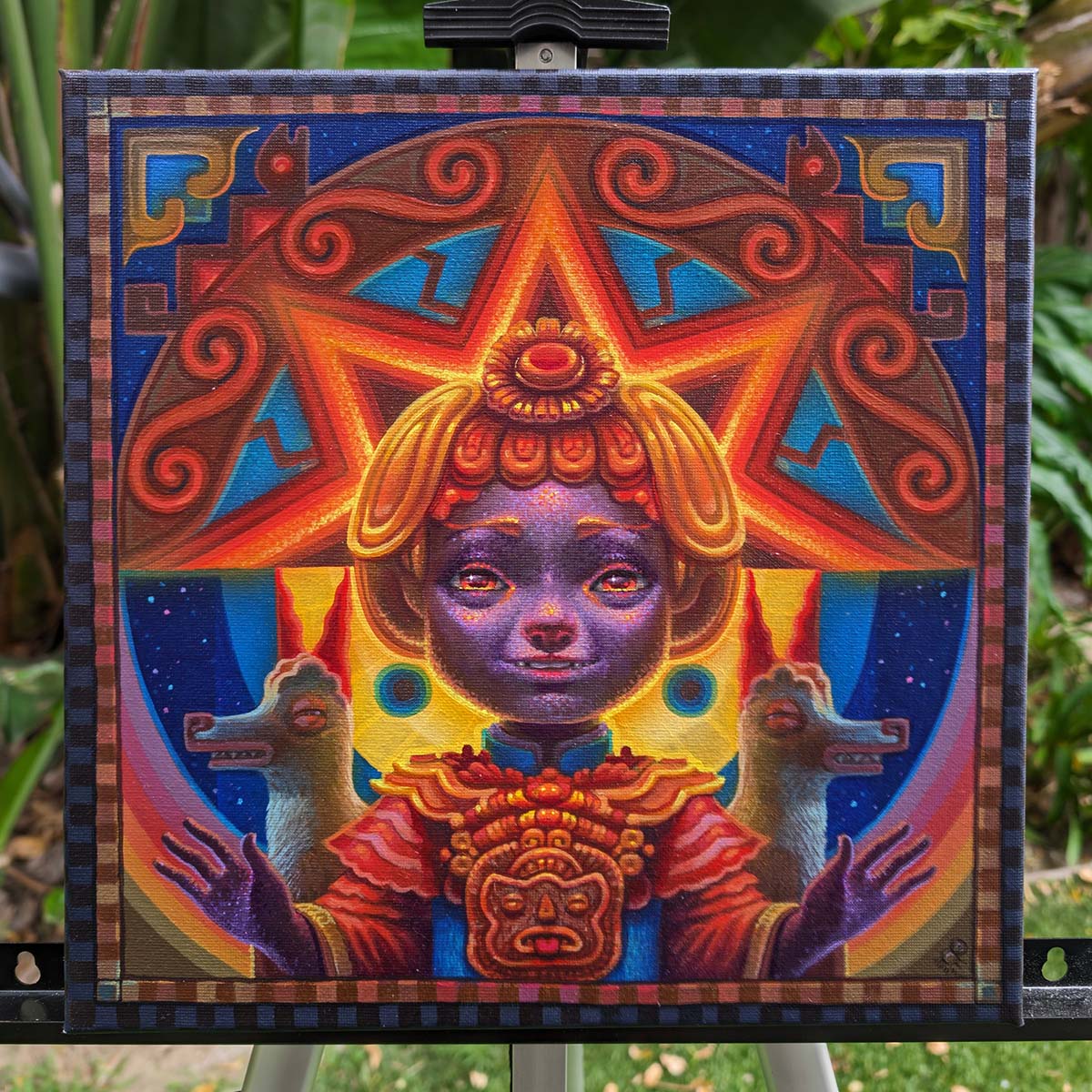 A view of the canvas an original oil painting of Inti as a child smiling in multicolor geometric orange and yellow and purple hues flanked by two symmetrical llamas with her arms out wide placed on an easel, outdoors.