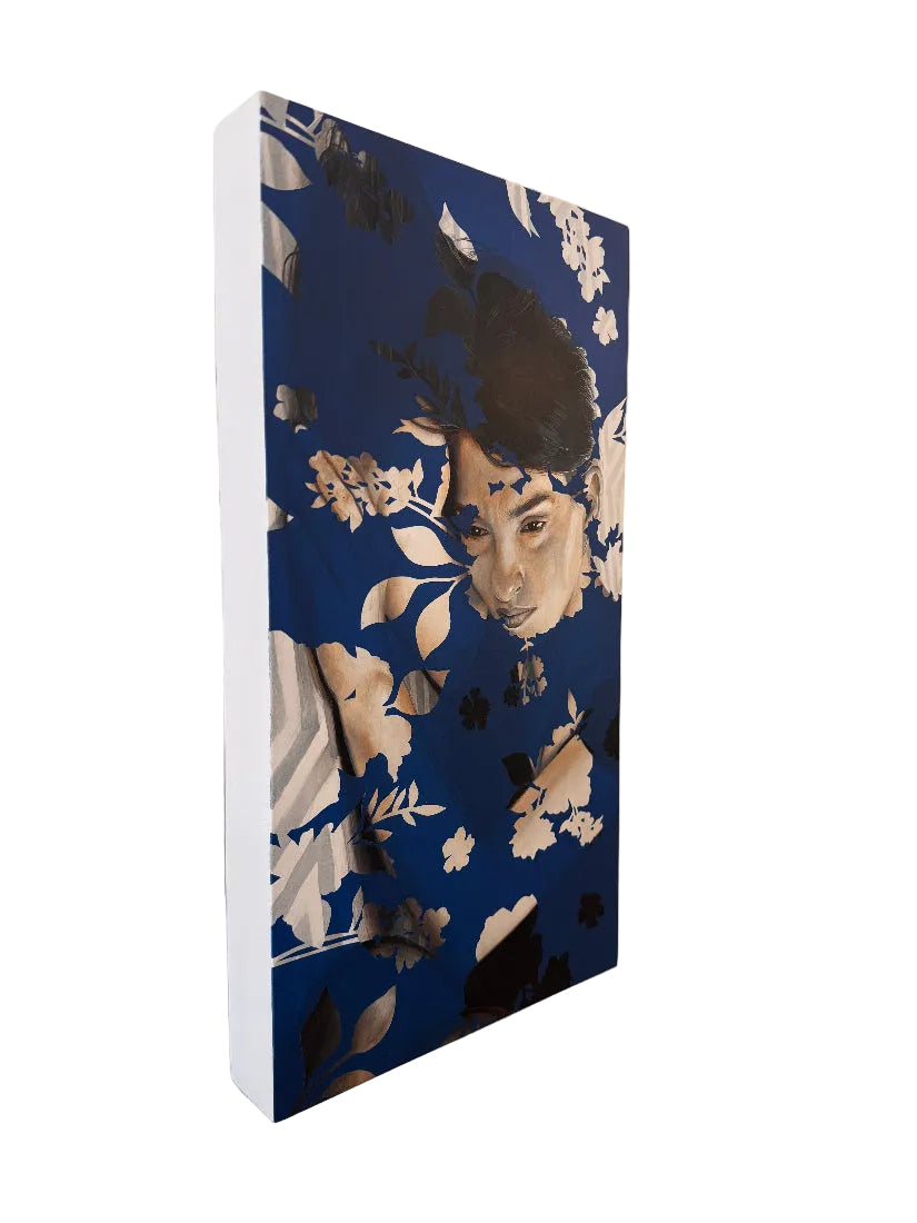 A vertical canvas wall art print featuring a stylized portrait of a woman's face blended with a dark blue floral pattern, shown hanging on a beige wall.