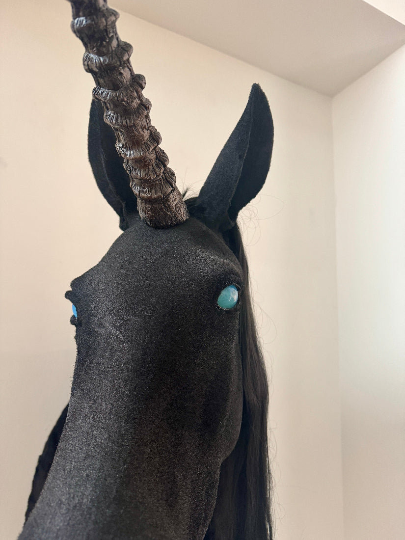 Unicorn head sculpture with dark gray body and black mane against a plain wall.