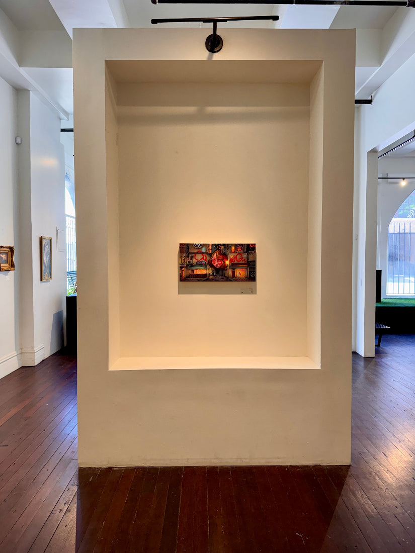 Art installation in a gallery with a framed piece on a white wall.