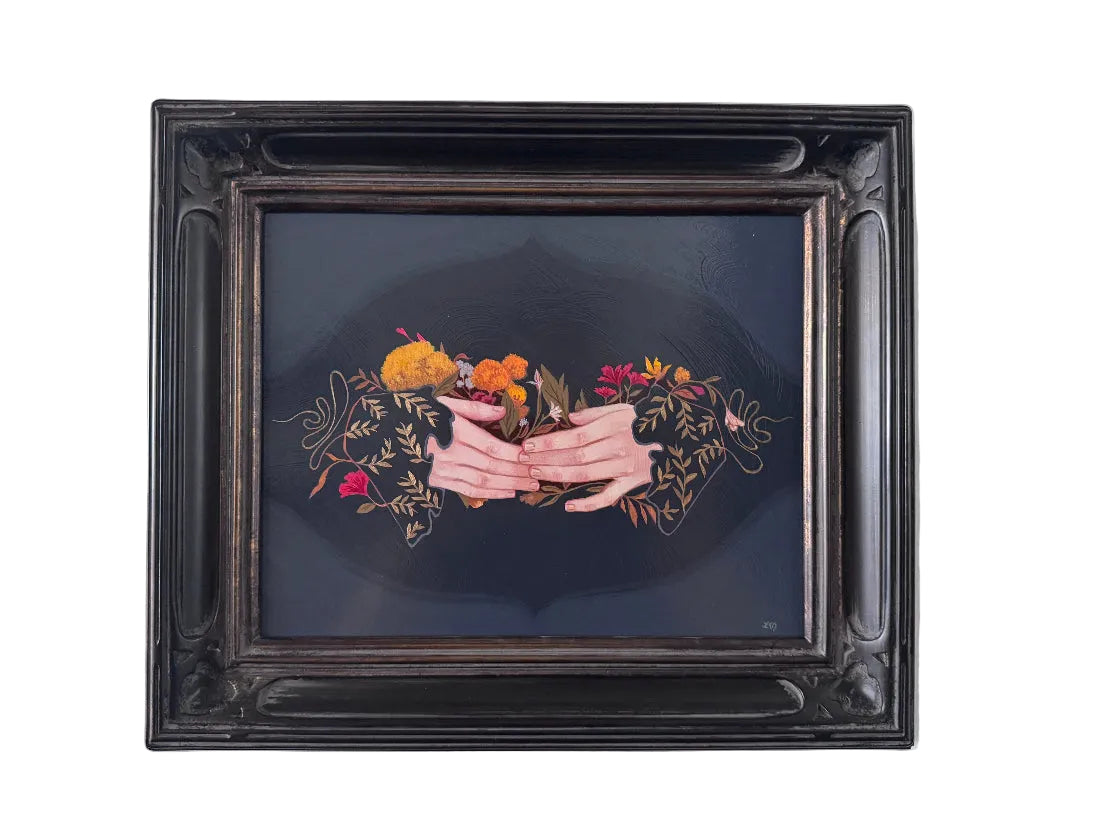 A framed painting featuring a dark illustration of two hands holding a bouquet of orange and red flowers, set within an ornate black frame and mounted on a light gray wall.