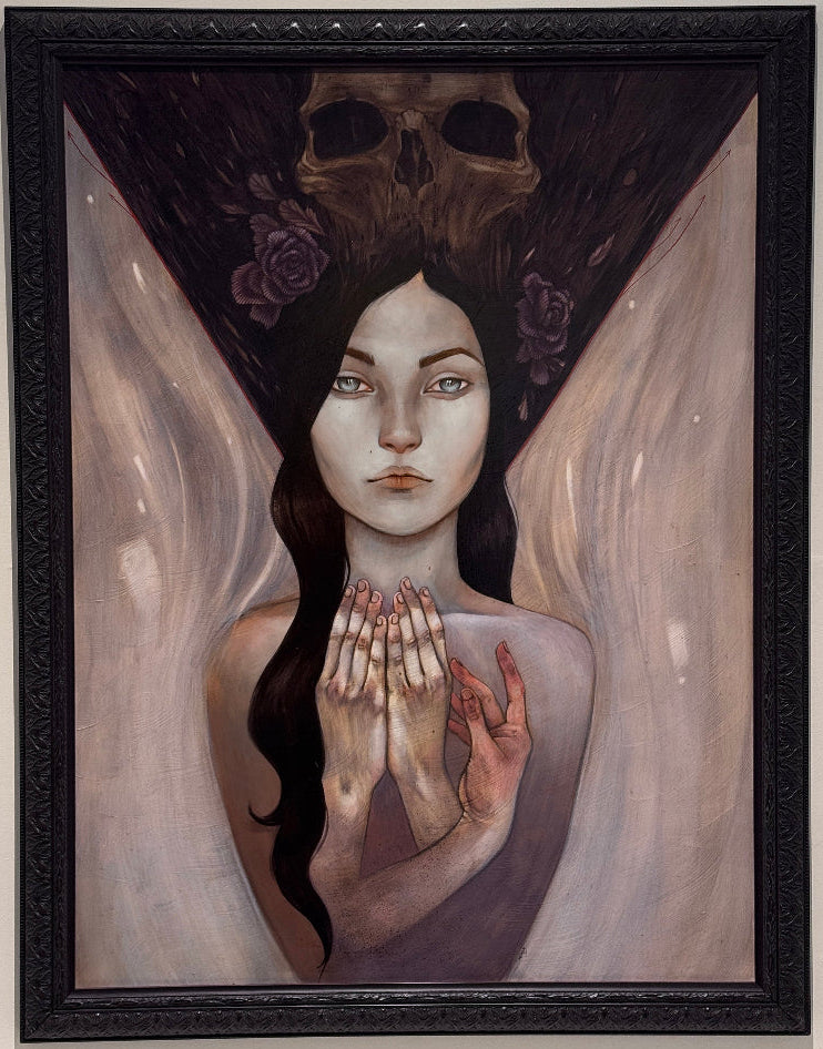 A framed surreal painting of a pale woman with clasped hands, a dark skull-like headpiece with roses, and flowing light drapery, displayed on a light wall.