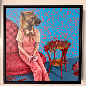 Framed artwork of a person with a hyena head in a pink dress sitting on a red chair against a blue patterned wall.