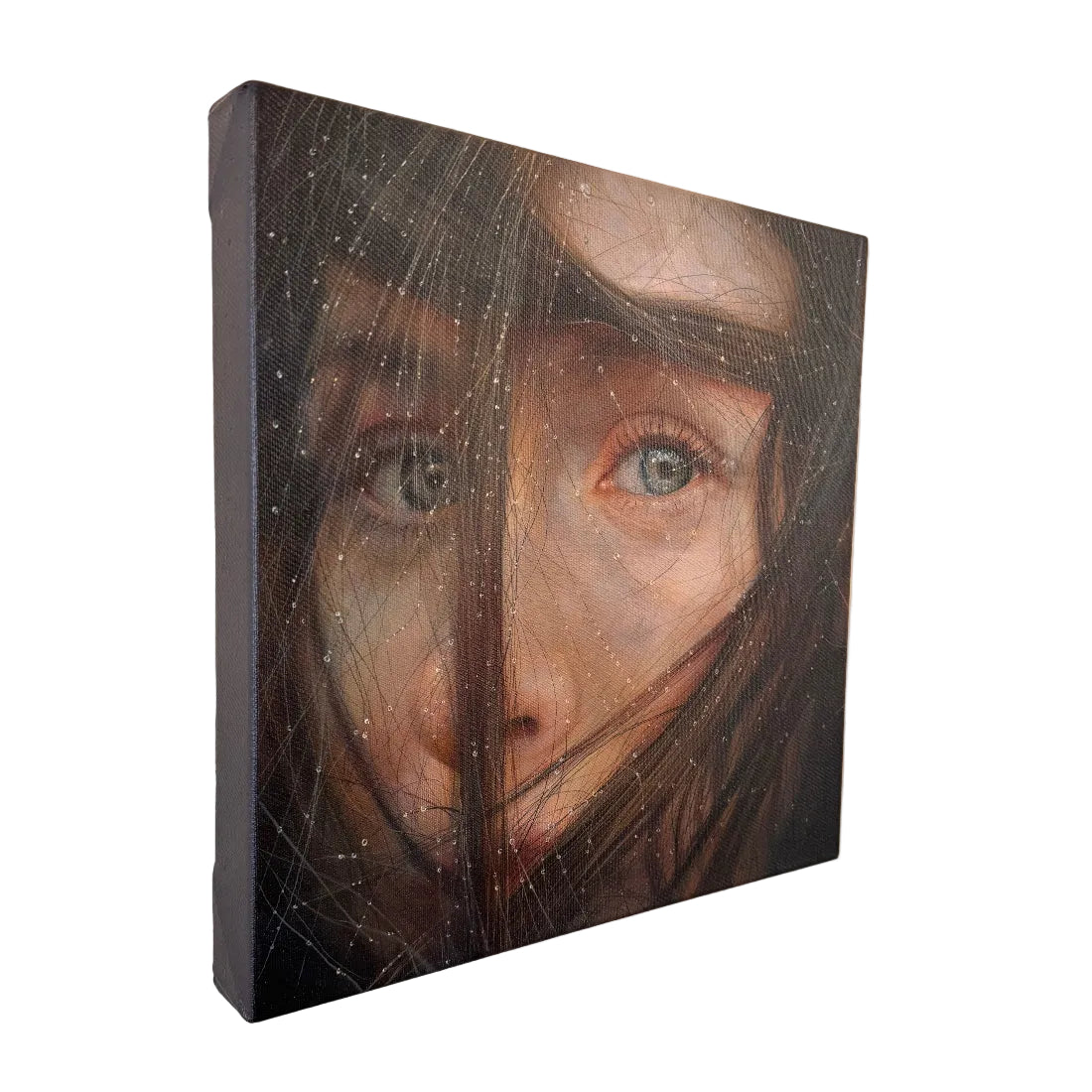 A square canvas wall art print featuring a close-up portrait of a woman's face obscured by dark hair and fine web-like lines, hanging on a light beige wall.