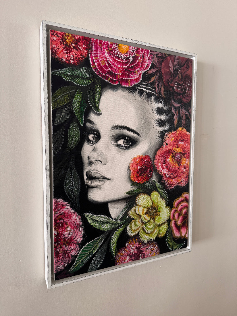 Framed artwork of a woman's face with colorful flowers on a beige wall