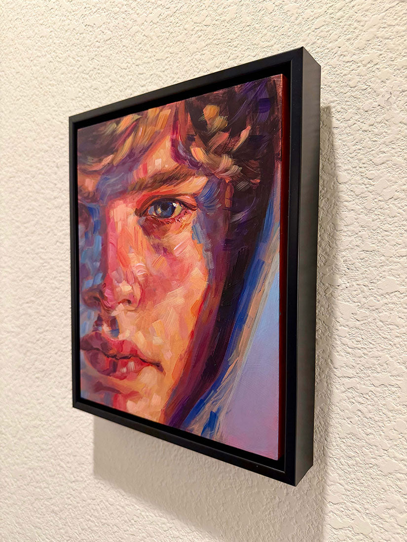 A framed portrait painting of a woman's face, shown hanging on a textured off-white wall. The artwork features expressive brushstrokes in red, orange, purple, blue, and pink, enclosed in a black frame.