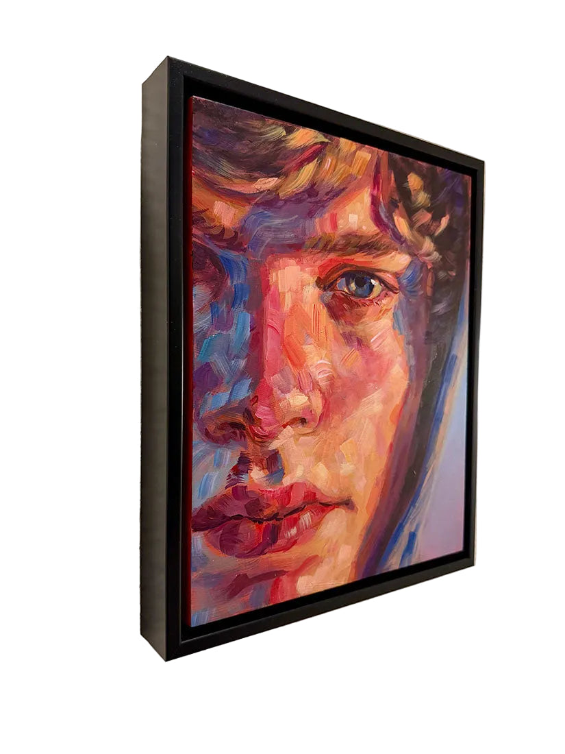 A framed portrait painting of a woman's face, rendered in expressive multicolored brushstrokes with prominent red, blue, purple, and peach tones, hanging on a textured off-white wall.