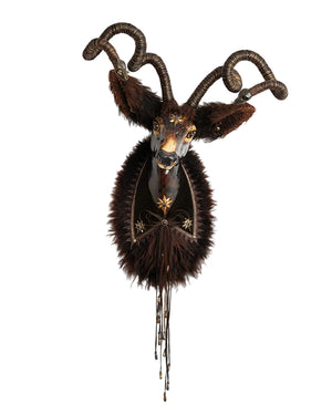A decorative taxidermy-style wall mount featuring a dark brown goat or ram head with curled horns, dark fur, and gold-toned embellishments on a plain white background.