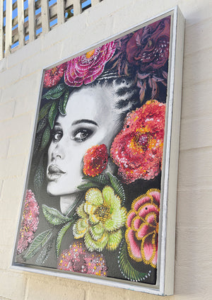 Framed artwork of a woman's face with colorful flowers on a wall.