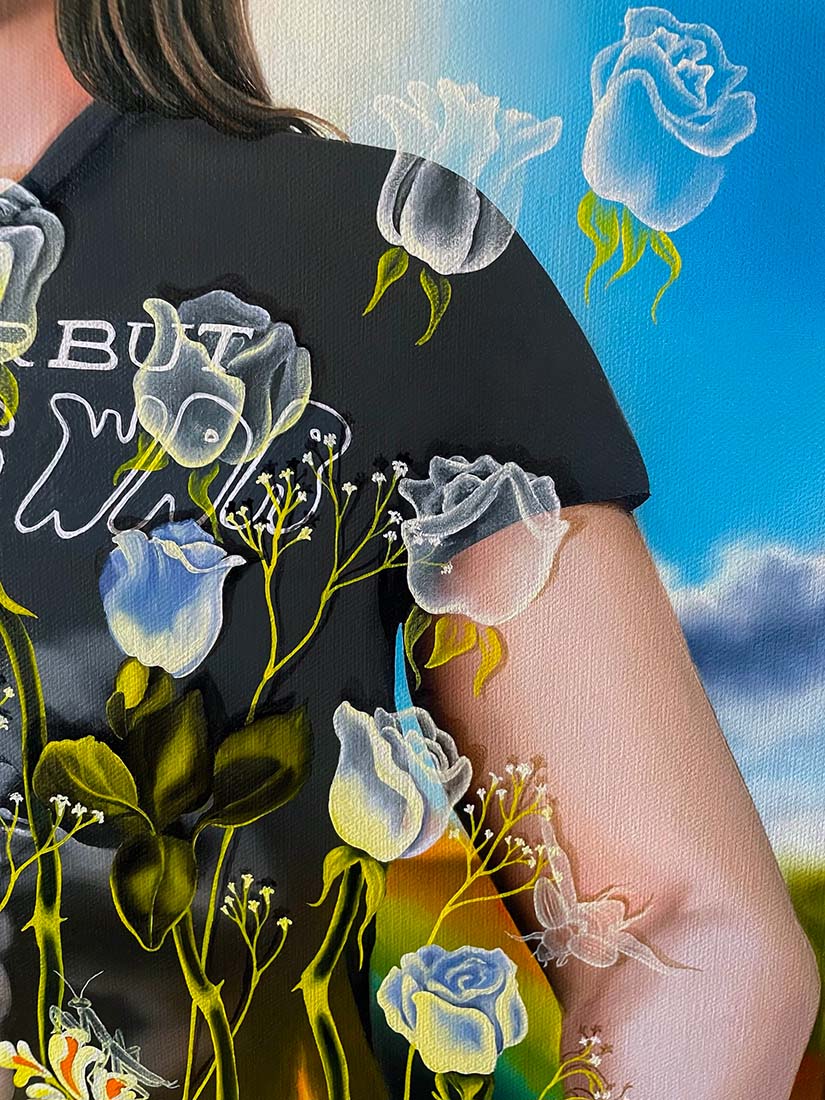 Person wearing a black shirt with floral designs and text, standing against a blue sky with clouds.