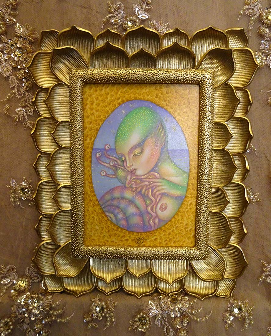 A framed art print featuring a stylized green alien or creature illustration inside an oval, surrounded by a textured gold frame with a lotus-like pattern, set against a brown background with decorative floral embellishments.